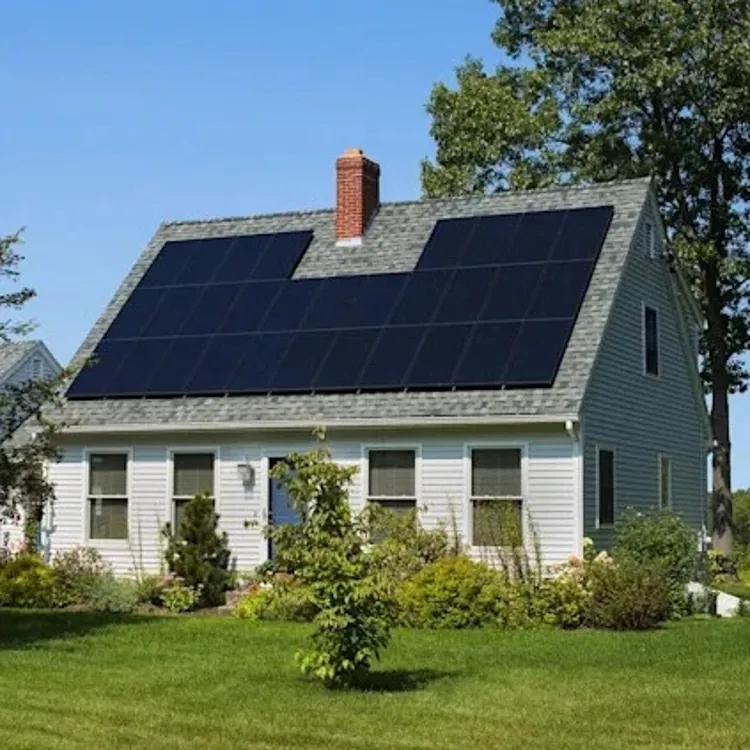 House with black solar panels on roof surrounded by green lawn and trees