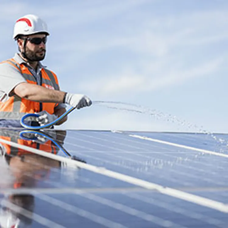 technician using a hose to spray solar panels with water