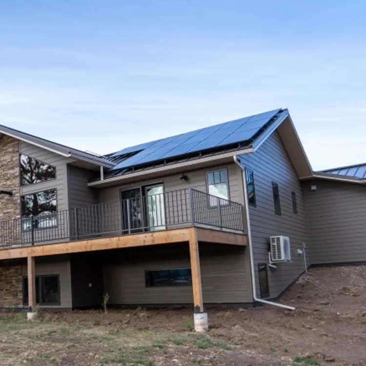 A modern house with rooftop solar panels and a large elevated deck in a rural area.