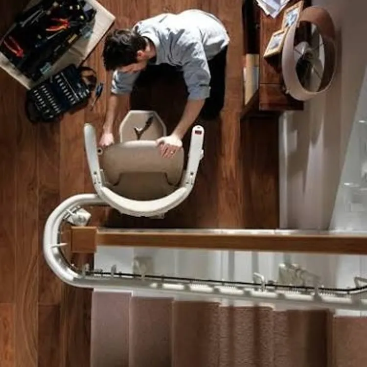 Technician installing a stairlift at the bottom of a residential staircase with tools nearby