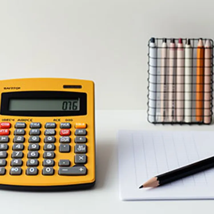 a yellow calculator beside a pencil on a notepad and a set of dermatograph pencils in different colors.