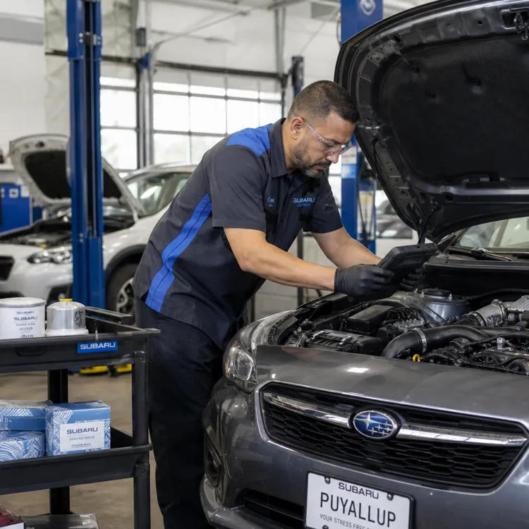 Mechanic working on Subaru car engine in a service center with parts cart nearby