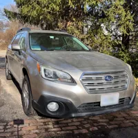 Silver car parked on a brick driveway surrounded by trees and suburban houses under a clear blue sky.