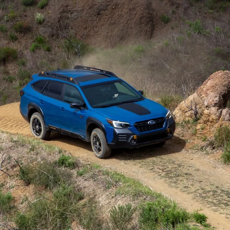 Blue SUV driving on a winding dirt road through a hilly, grassy landscape