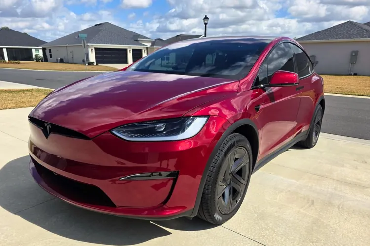 Red electric car parked on a driveway in a suburban neighborhood under a partly cloudy sky.