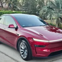 Red electric vehicle parked on a driveway surrounded by palm trees and greenery.