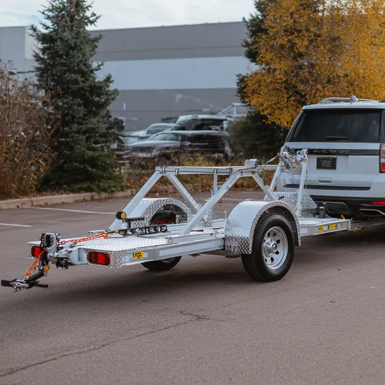 Silver SUV towing an empty metal car trailer in a parking lot with autumn trees nearby