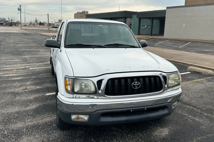 White pickup truck parked in an empty urban parking lot with an overcast sky.
