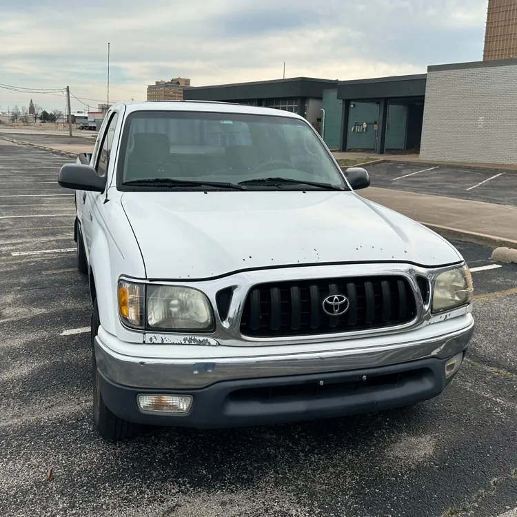 White pickup truck parked in an empty urban parking lot with an overcast sky.