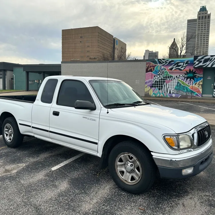 White pickup truck parked in an urban setting with a colorful graffiti wall and tall buildings in the background.
