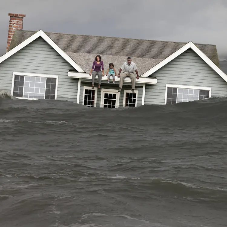 Three people sitting on the roof of a house surrounded by floodwaters