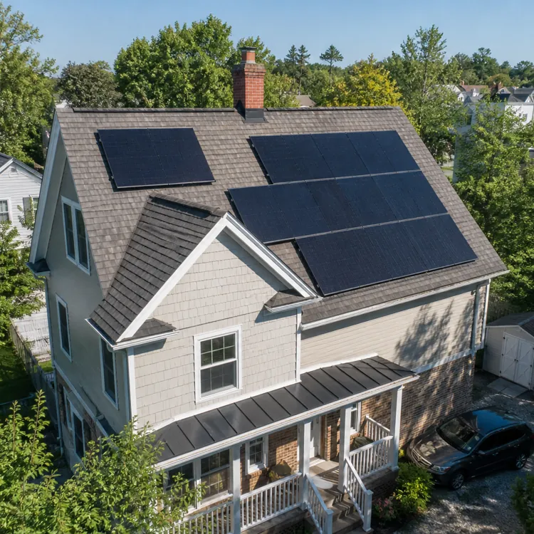 House with multiple solar panels on roof surrounded by trees and neighboring homes