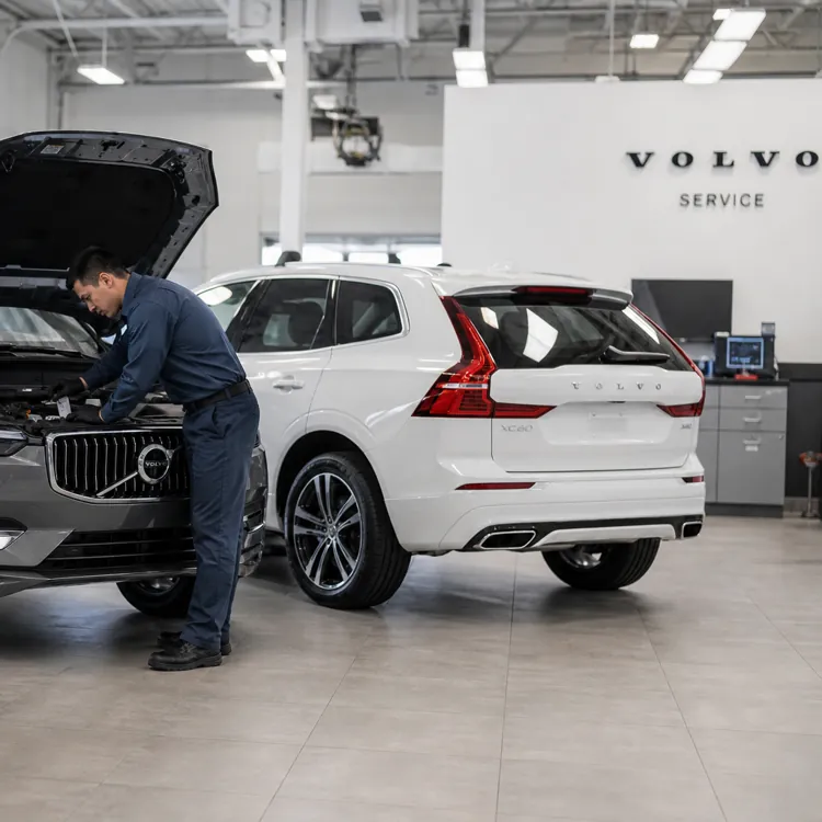 Mechanic working on a silver Volvo SUV with another white Volvo parked in a service center