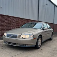 Beige sedan parked in front of a brick wall and metal warehouse.