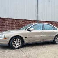 Beige sedan parked in front of a brick wall and metal building in a parking lot.