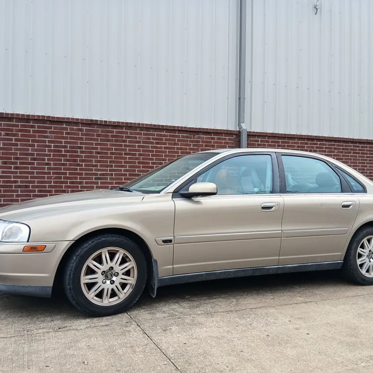 Beige sedan parked in front of a brick wall and metal building in a parking lot.