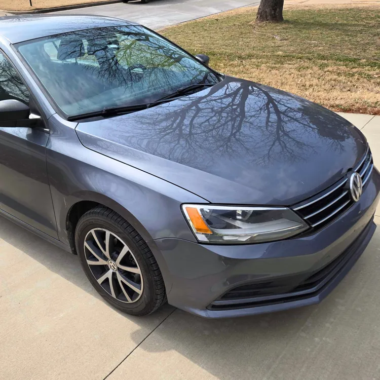 Gray sedan parked on a concrete driveway with a grassy area and tree in the background.
