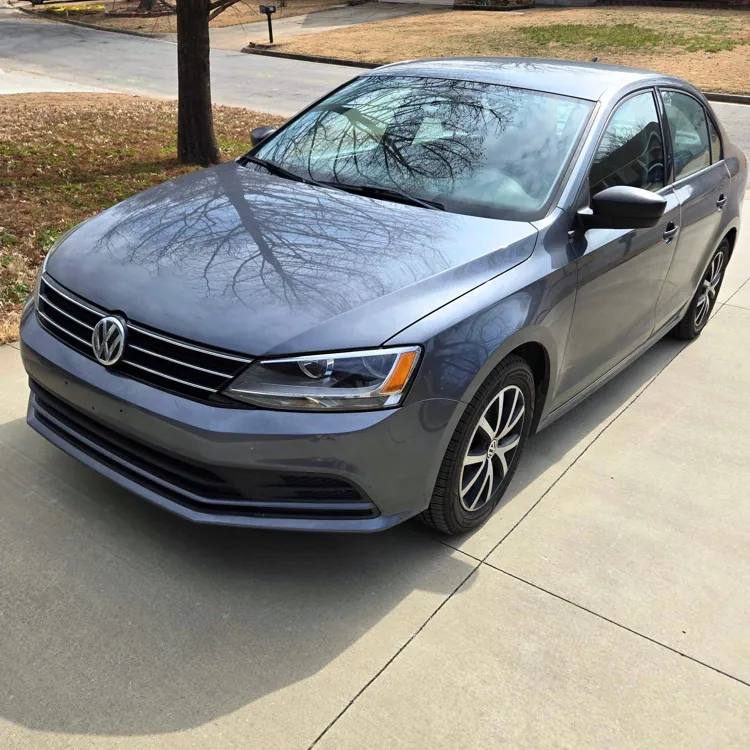 Gray Volkswagen sedan parked on a concrete driveway in a suburban neighborhood.