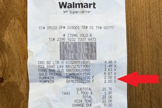 Walmart receipt listing purchased items including pumpkins, placed on a wooden table with a red arrow pointing
