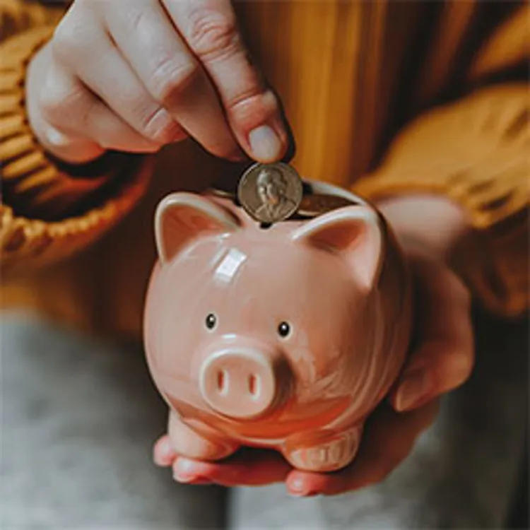 person holding and dropping coins on to a ceramic piggybank