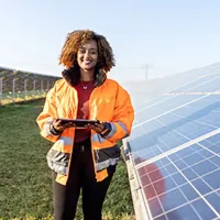woman in reflective clothing holding a tablet pc standing by solar grid at solar farm