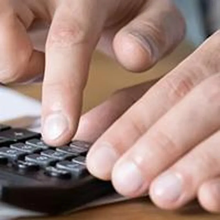 pair of hands using a calculator on top of pile of papers