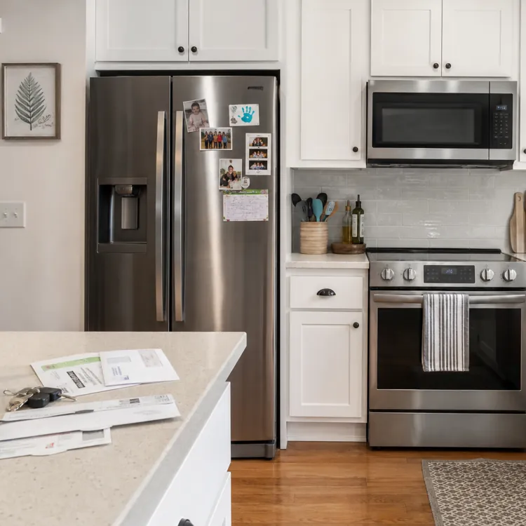Modern kitchen with stainless steel appliances, white cabinets, and mail on the counter