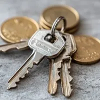 a close-up of metal keys on a keyring lying near scattered gold-colored coins