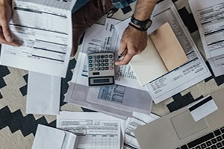 man looking over a lot of bills with calculator and computer