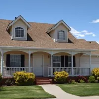 a beige two-story house with a brown shingle roof and two arched dormer windows