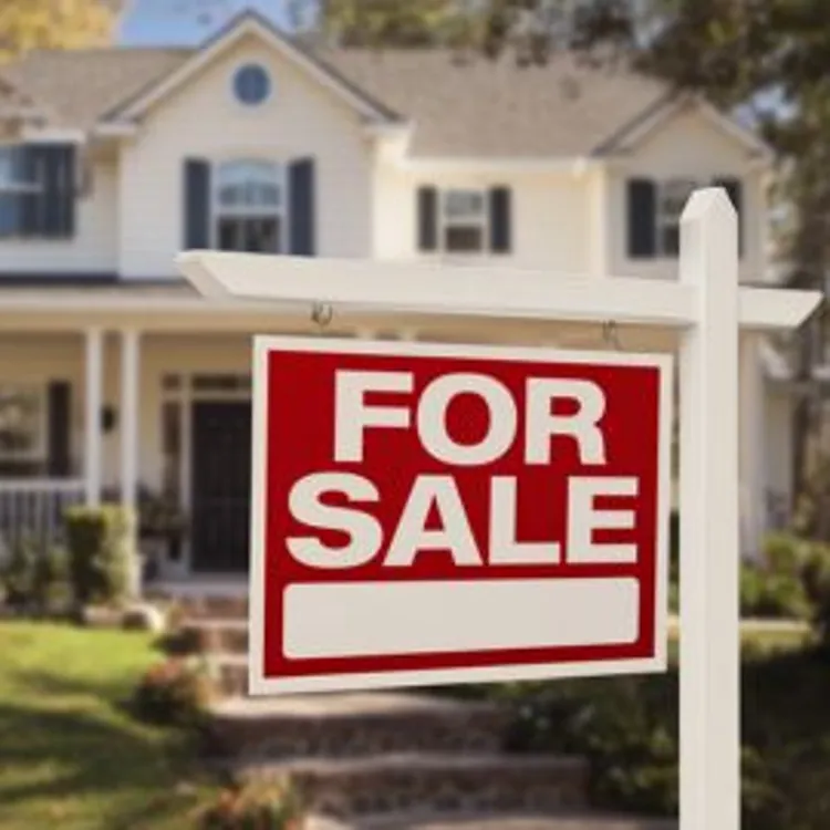 a for sale sign hung in front of a two story house