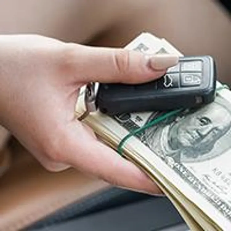 woman holding money and keys in car