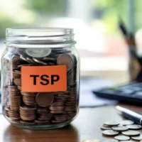 a coin-filled glass jar labeled with tsp placed on flat surface with a pen and some coins
