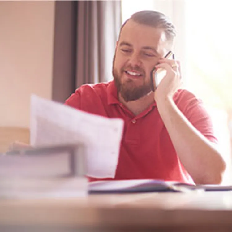 man talking on a phone smiling with paper on his hand