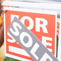 man putting sold sign on a for sale sign in front of house