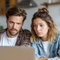 a man and a woman looking at a laptop with a serious expression in their faces