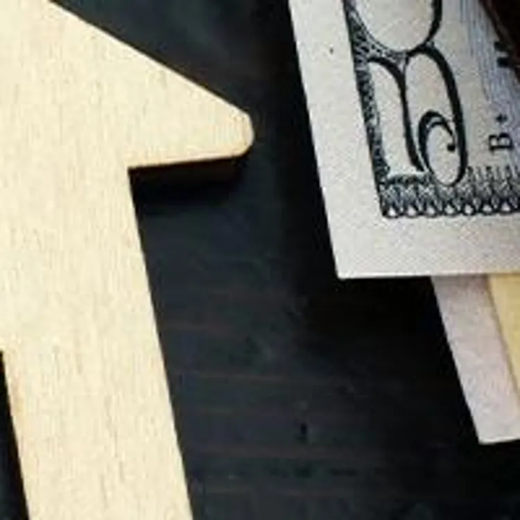 wooden house model with property tax sign and on the right side a wallet with money showing