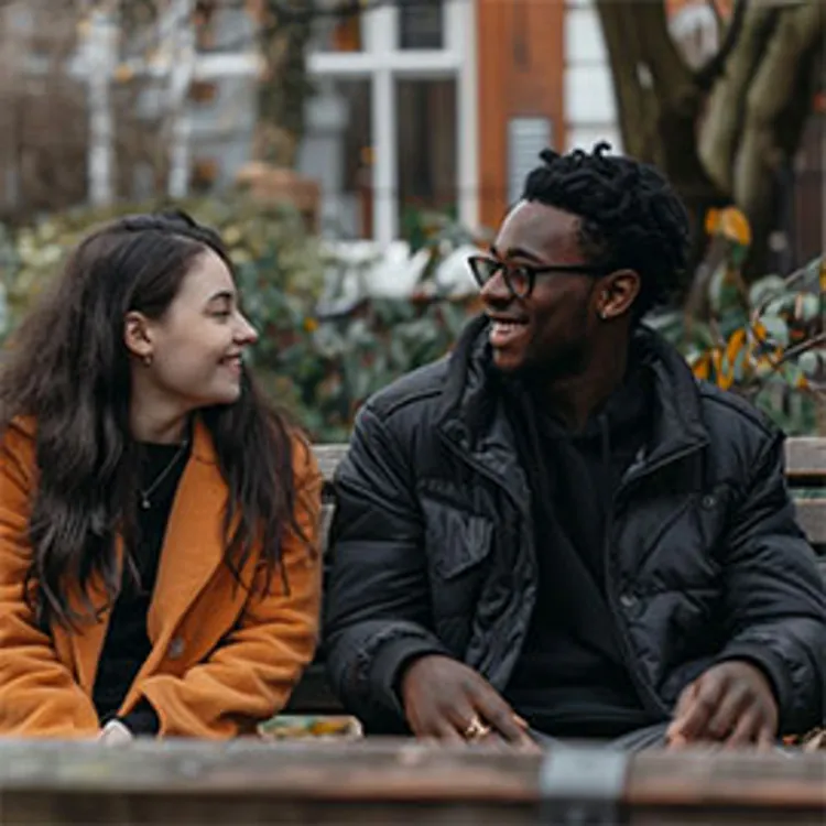 man and woman chatting while seated on a bench