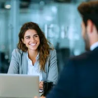 a man and a woman in business attire sitting across from each other with a laptop between them