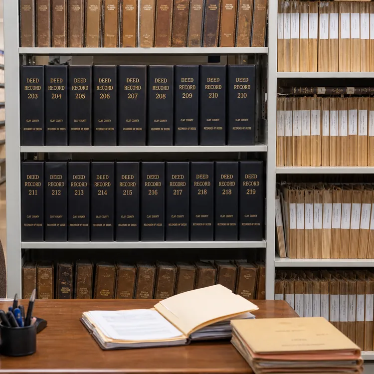 Office desk with computer and open files in front of shelves filled with deed record books and folders