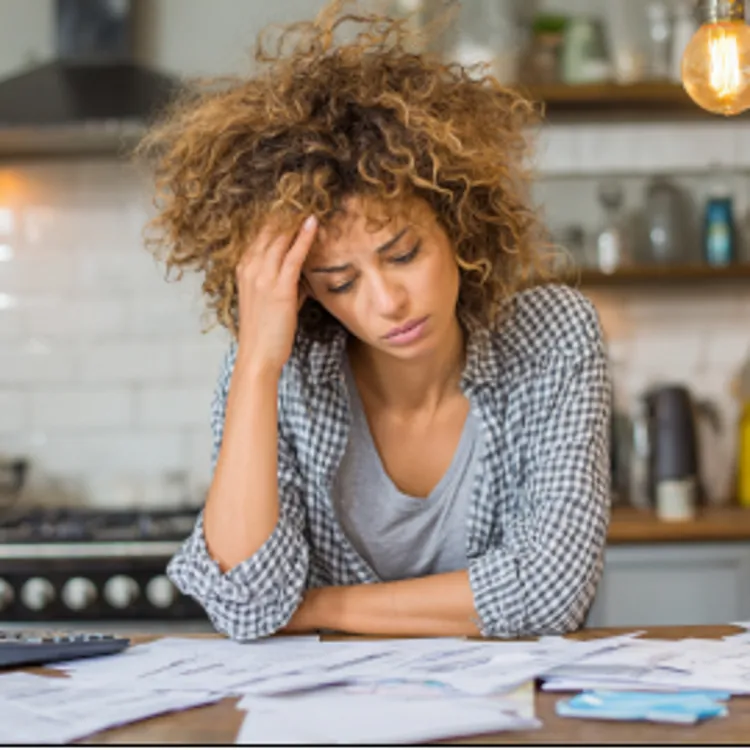 woman worriedly looking at bills on a table while holding her head with one hand
