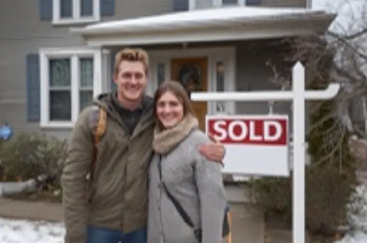 young couple standing in front of a new home with a sold sign in the yard