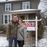 young couple standing in front of a new home with a sold sign in the yard