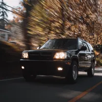 Black SUV driving on a suburban road with blurred autumn trees in the background.