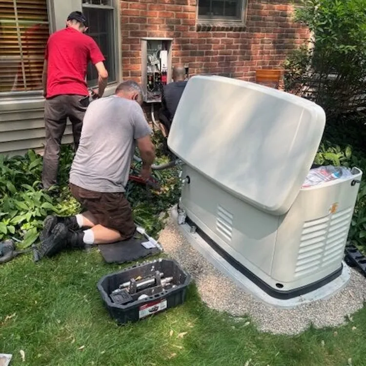 Two technicians installing a standby generator next to a brick house with tools on the grass