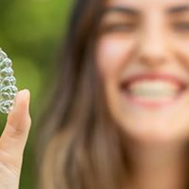 woman smiling while holding clear aligner