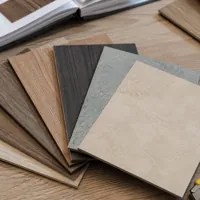 Assorted flooring samples fanned out on a wooden table with a utility knife and catalog nearby
