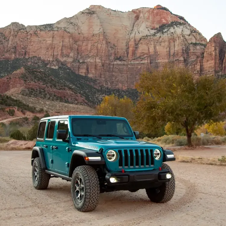 Blue SUV parked on a dirt lot with large rocky mountains and trees in the background